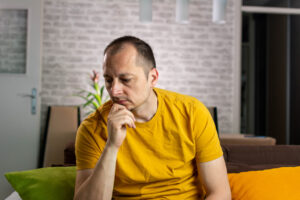Unhappy caucasian male sitting on living room couch suffering from low testosterone.