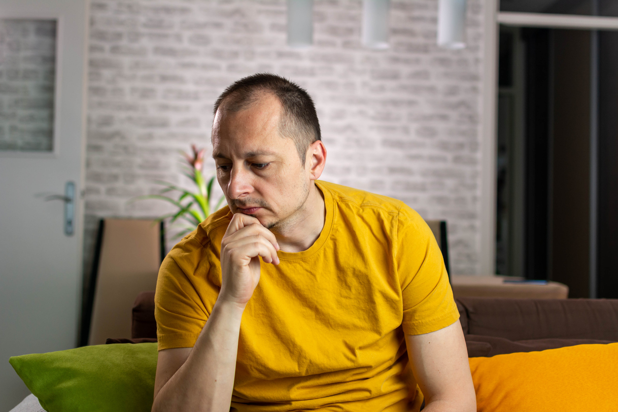 Unhappy caucasian male sitting on living room couch suffering from low testosterone.